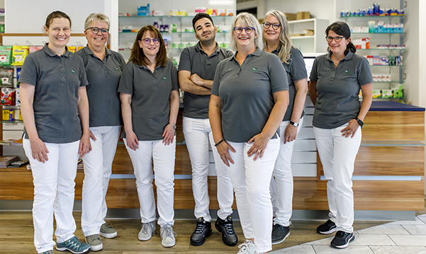 Das Team der Martinus Apotheke in Trier steht zusammen in der Apotheke, im Hintergrund stehen Medikamentenregale.