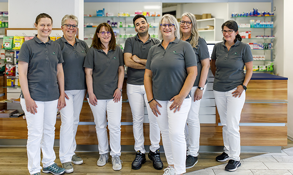 Das Team der Martinus Apotheke in Trier steht zusammen in der Apotheke, im Hintergrund stehen Medikamentenregale.